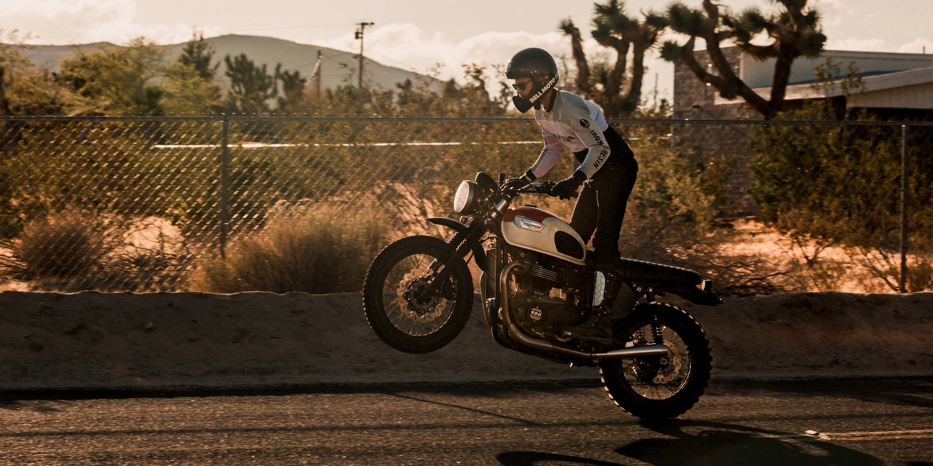 Triumph motorcycle performing a wheelie, featuring a British Customs Predator Carbon exhaust—now 25% off in the Mid Year Exhaust Closeout.